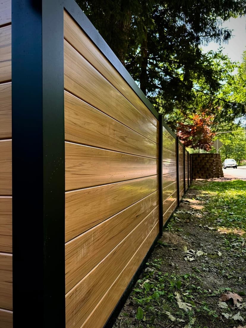 Modern wooden fence with black metal accents, framed by lush greenery and sunlight.