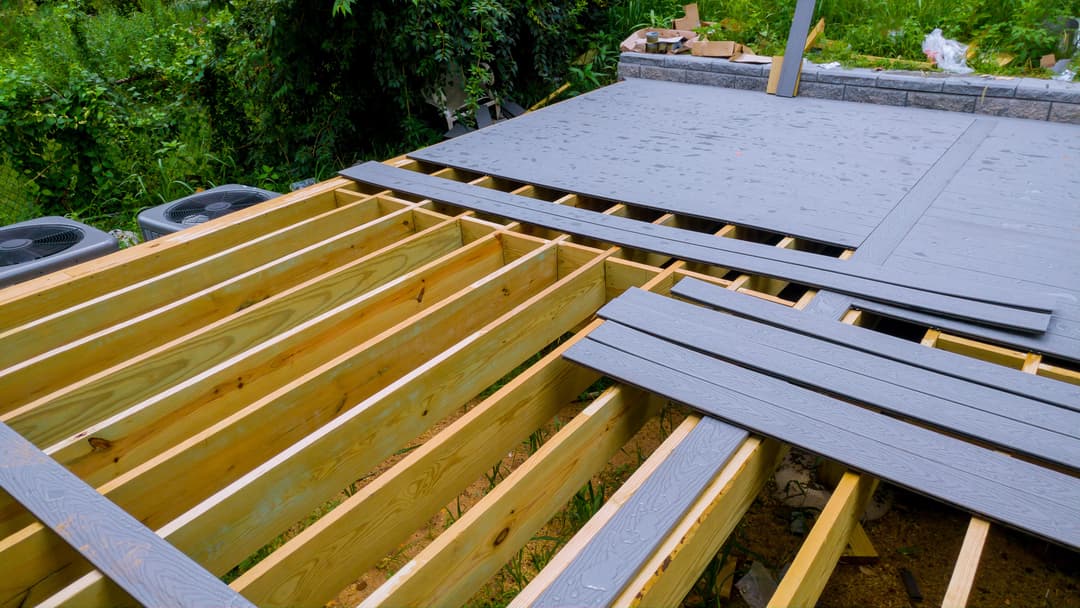 Construction of a wooden deck with gray planks and visible support beams.