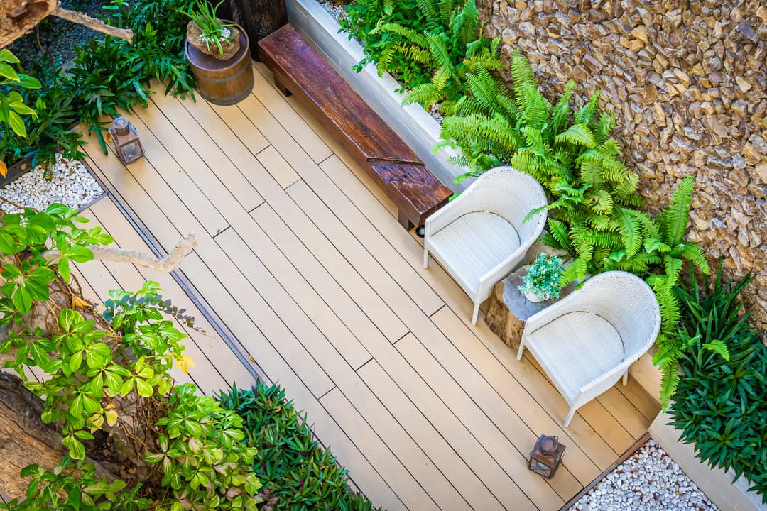 Serene outdoor garden with wooden deck, white chairs, plants, and decorative lanterns.