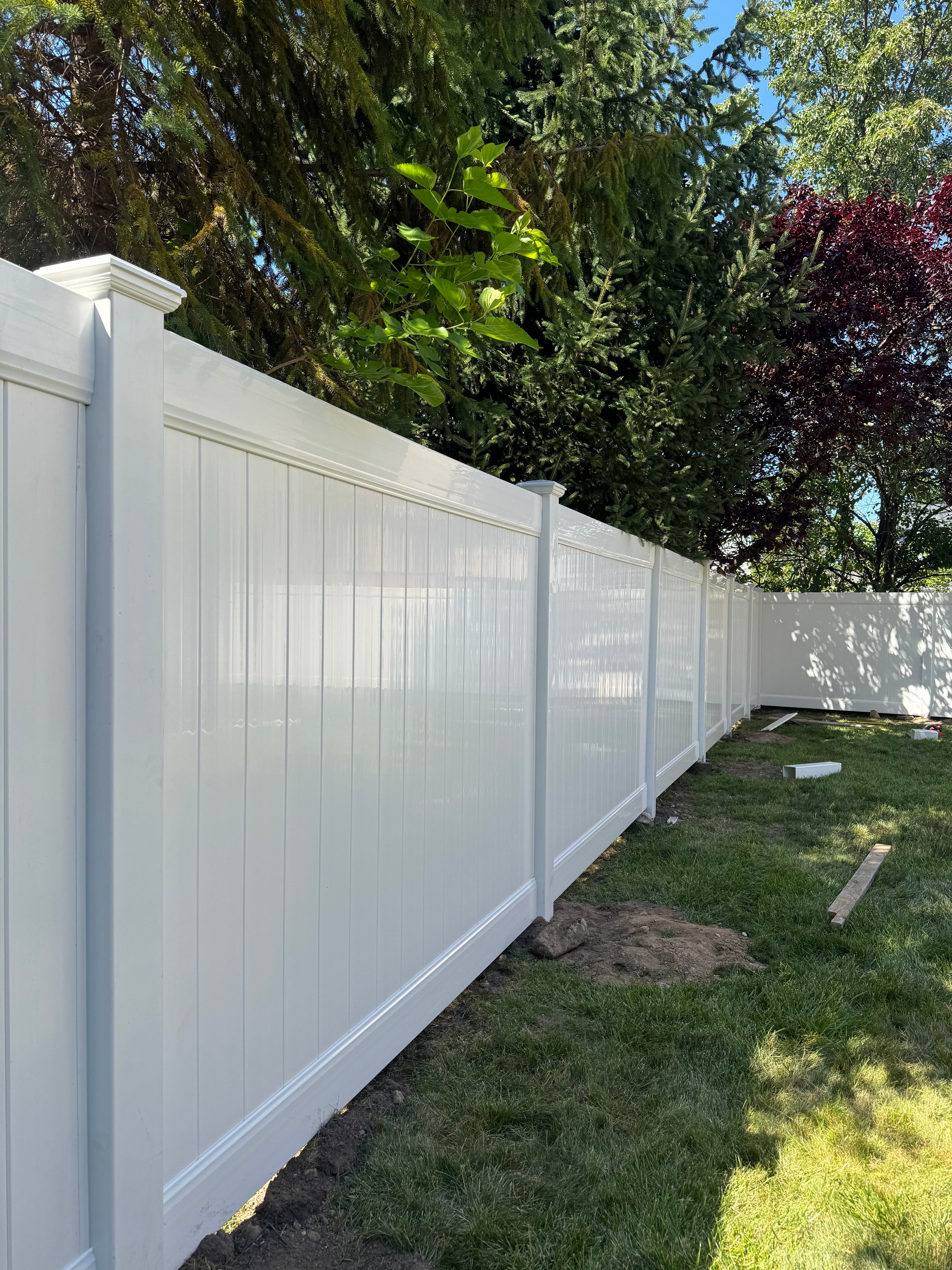 White vinyl fence installed in a backyard surrounded by trees under a clear blue sky.