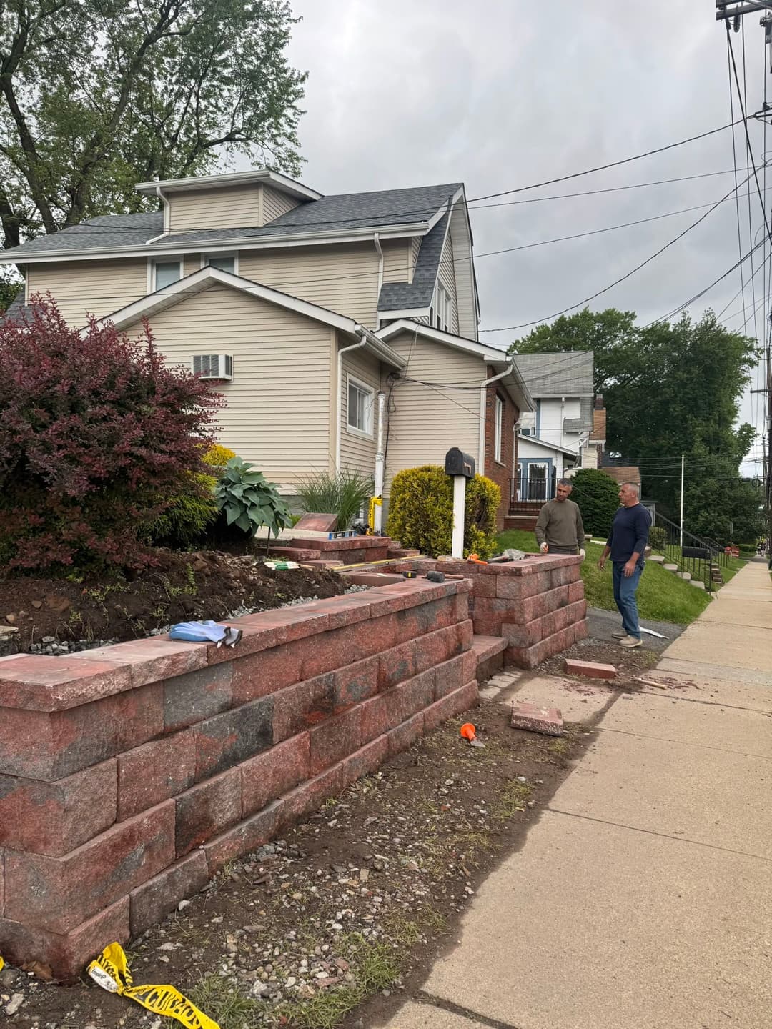 Home renovation with retaining wall landscaping and workers on a residential street.