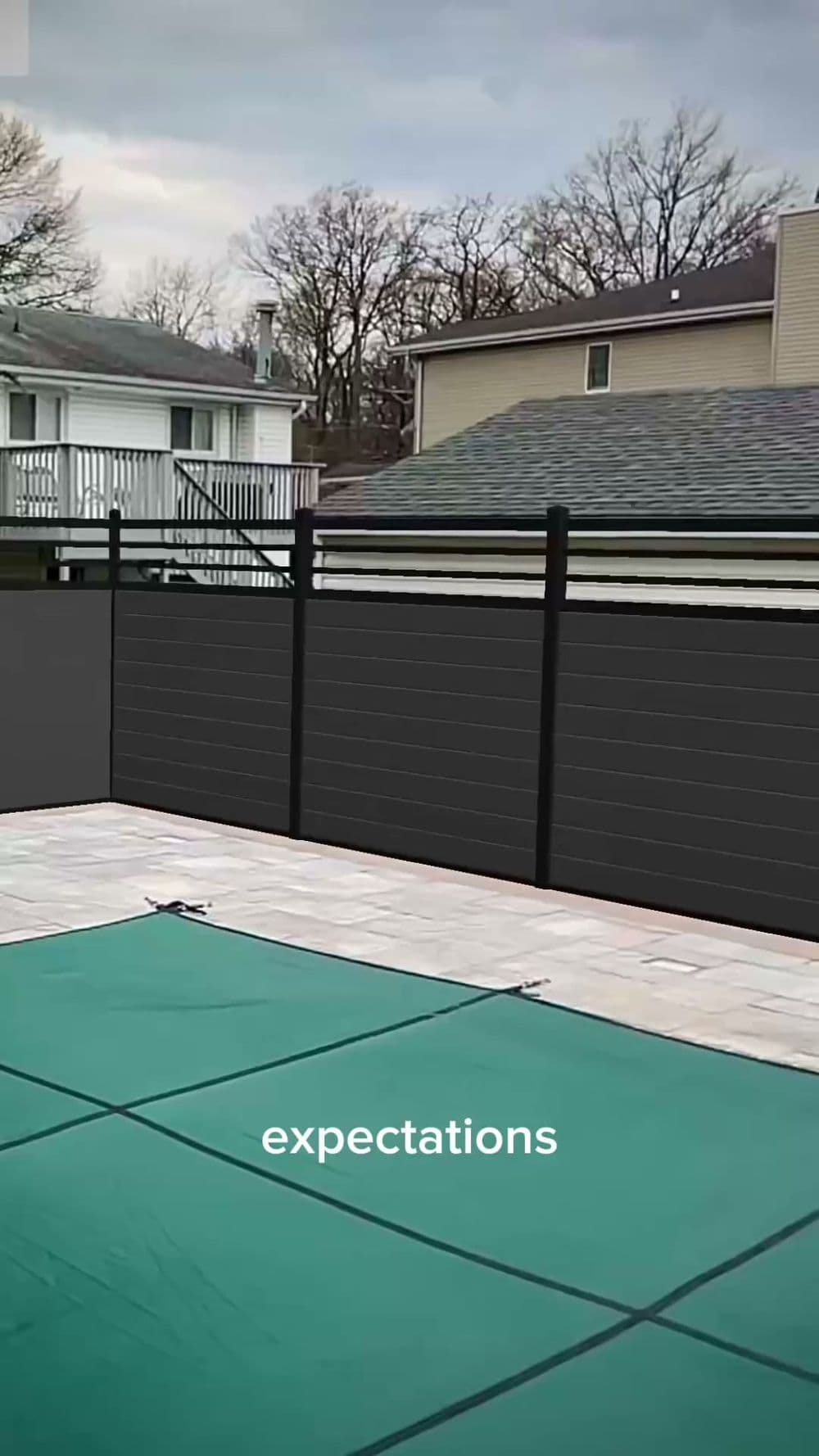 Backyard pool covered with a green safety cover and gray fencing in a suburban setting.