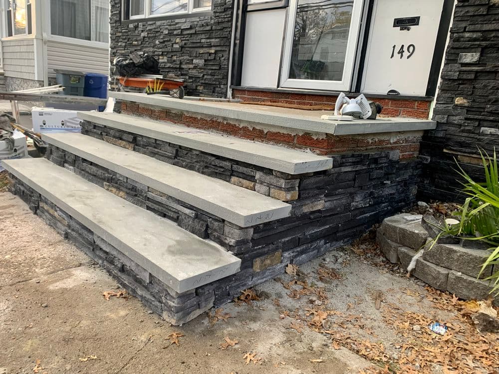 Concrete steps with stonework design leading to a house entrance, featuring landscape details.