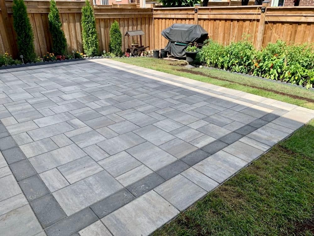 Modern backyard patio with gray stone pavers and landscaped garden features.