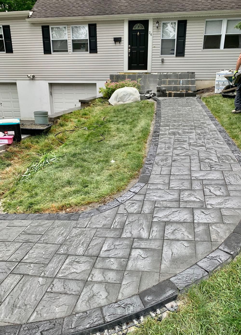 Patterned pavers walkway leading to a house, surrounded by green grass and landscaping.