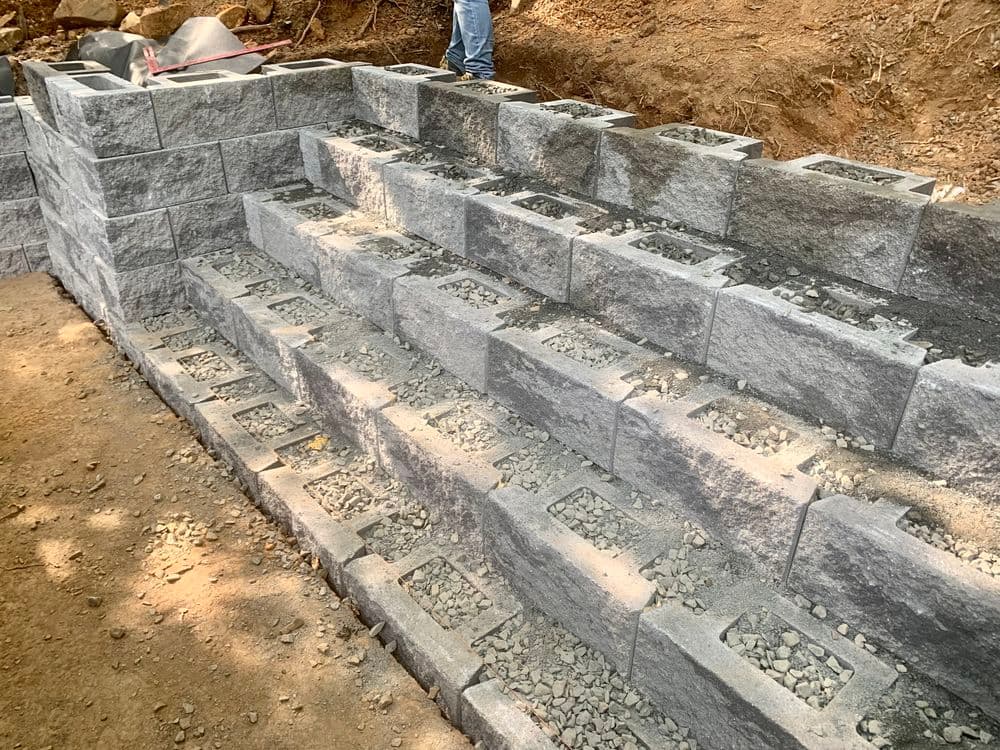 Gray concrete block steps under construction, featuring leveled gravel on a dirt path.