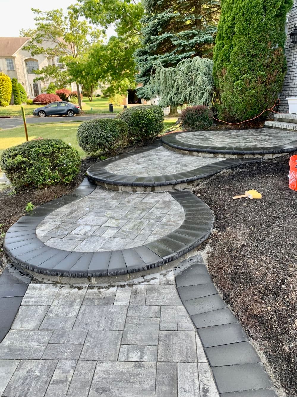 Curved stone pathway with landscaped grass and shrubs in a residential garden.