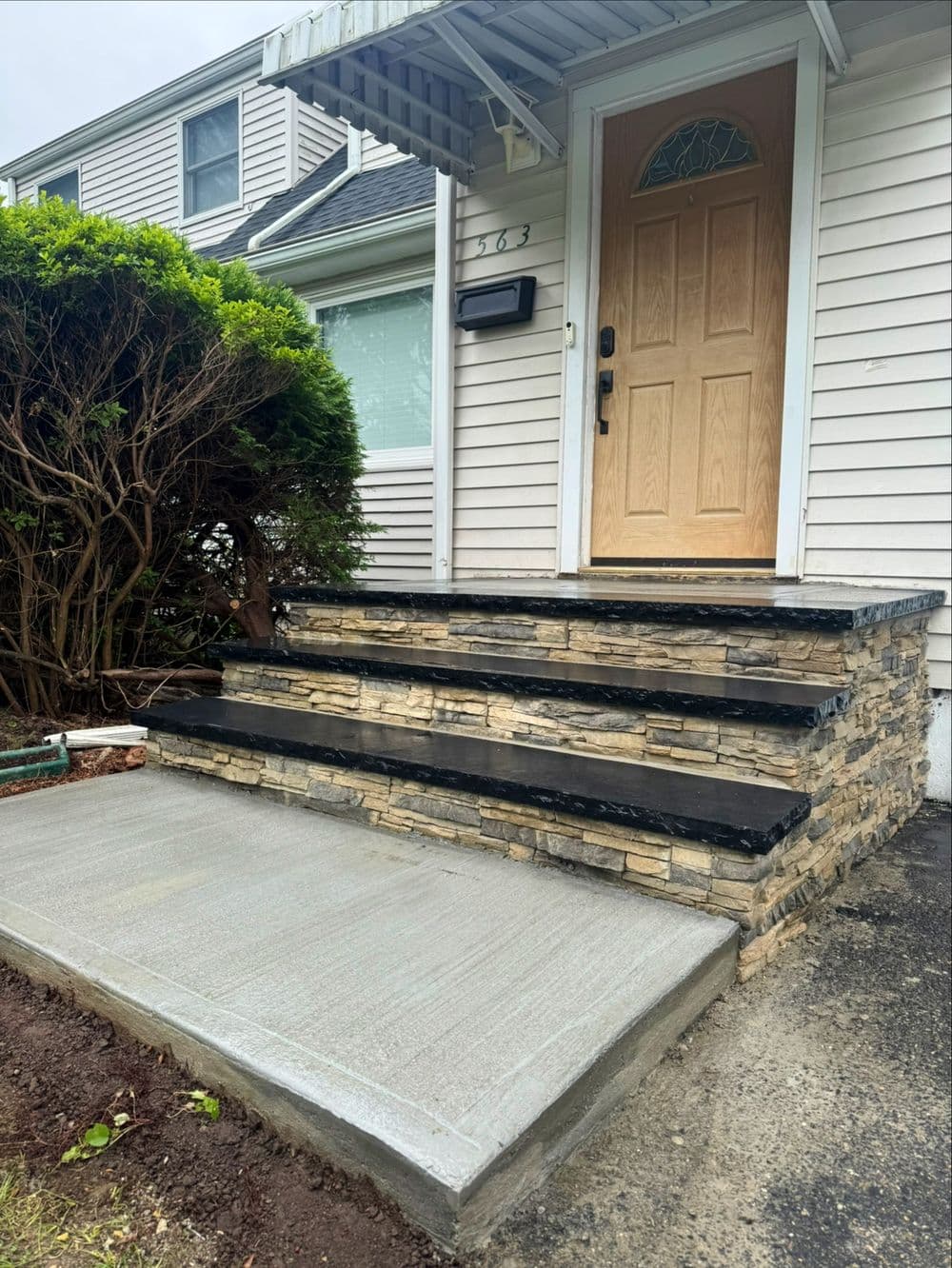Front entrance with stone steps, wood door, and newly paved concrete walkway.