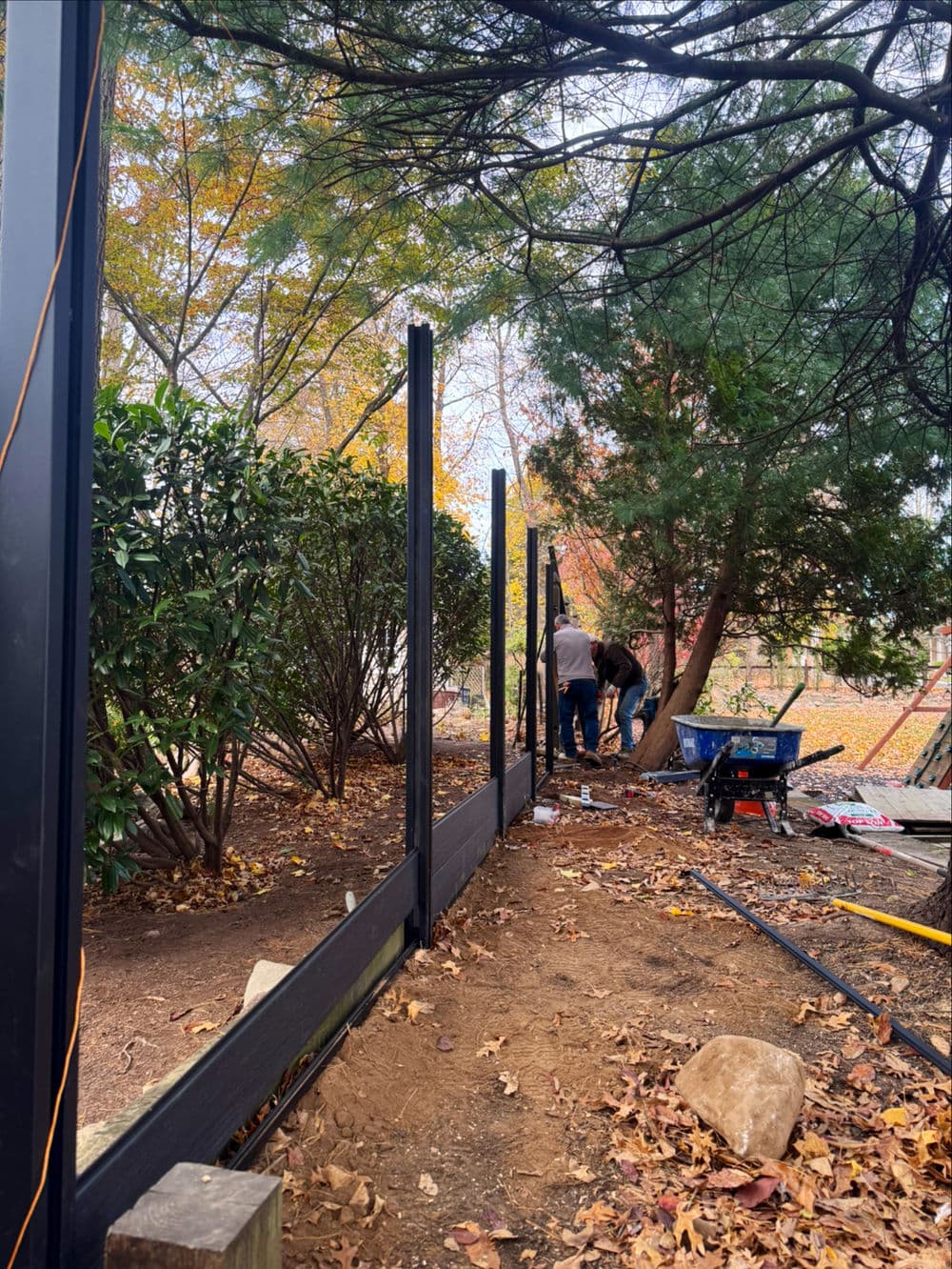 Workers installing a fence in a garden surrounded by autumn foliage and trees.