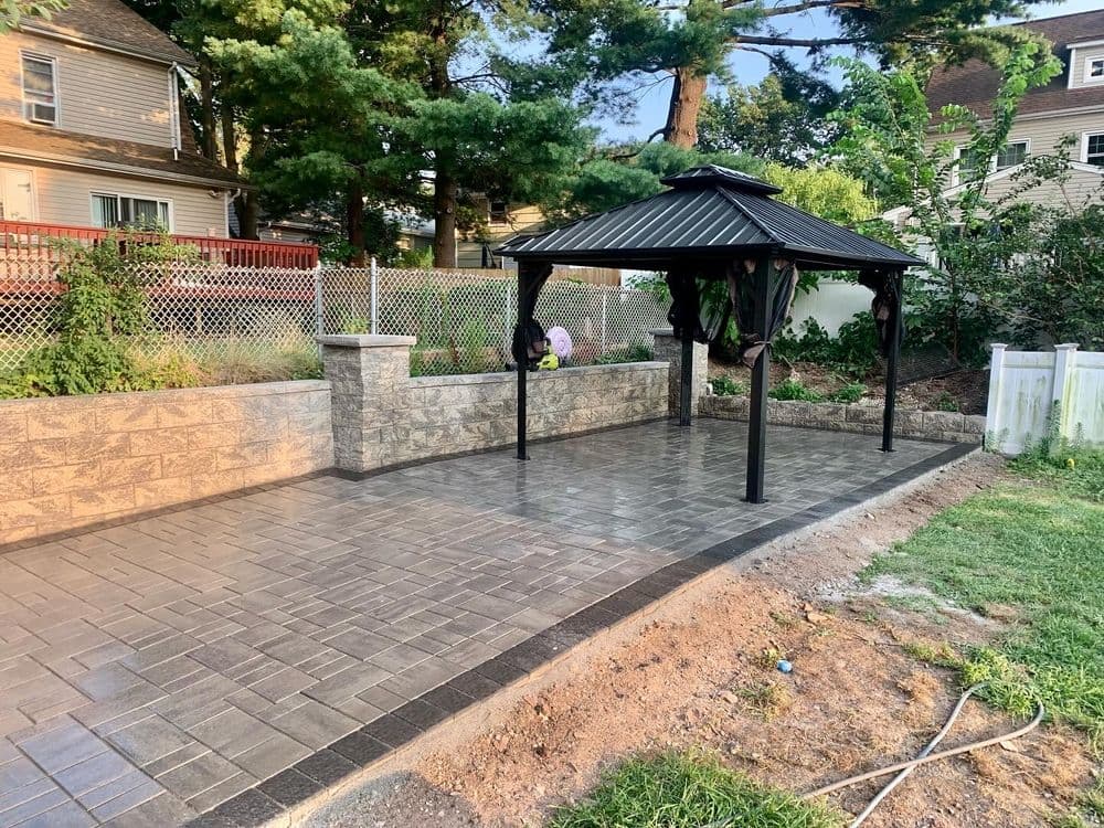 Paved backyard patio with gazebo and stone walls in a residential setting.