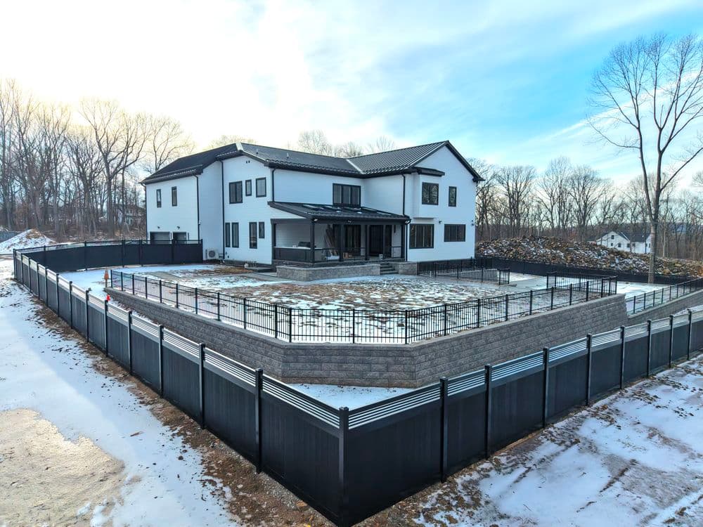 Modern two-story house with a spacious fenced yard and snowy landscape.