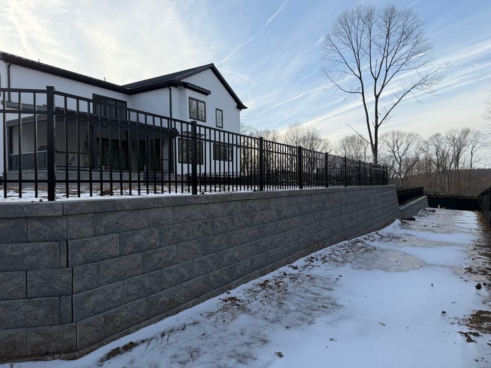 Modern home with black fencing and stone retaining wall in snowy landscape.