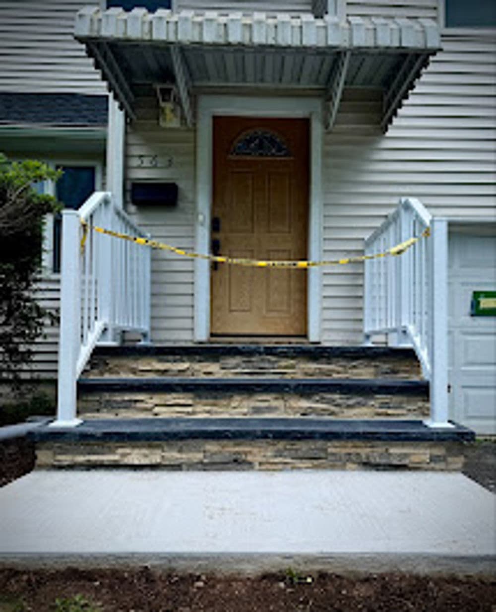 Front entrance with a wooden door and blocked stairs, marked with caution tape for safety.