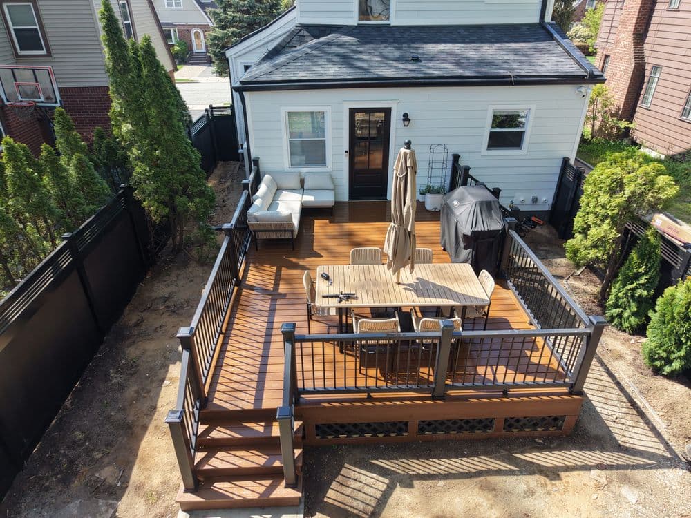 Aerial view of backyard deck with seating, dining table, patio umbrella, and grill.